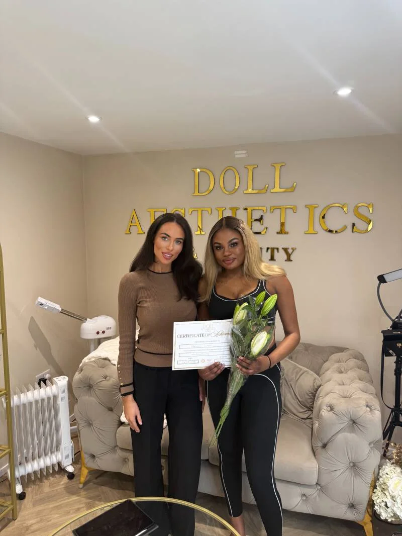 Two Doll Academy graduates holding a certificate and flowers in the West Mersea clinic
