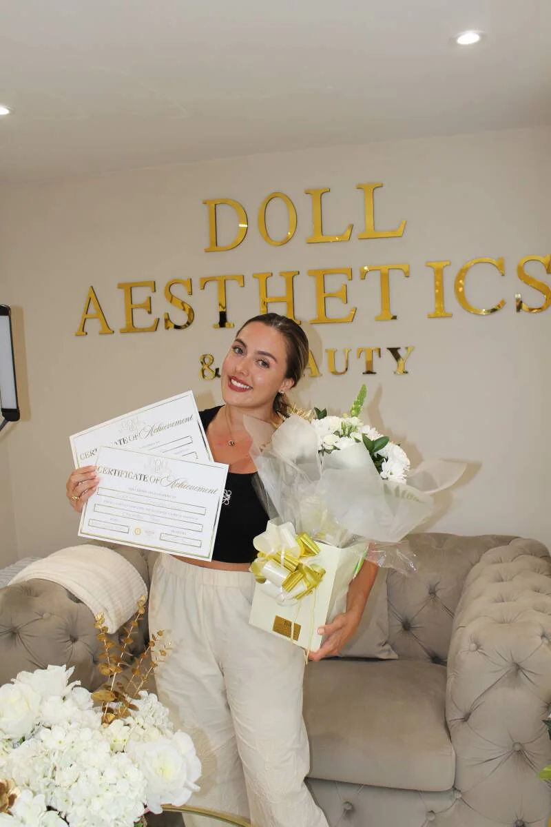 Doll Academy graduate holding her certificate and flowers in the clinic
