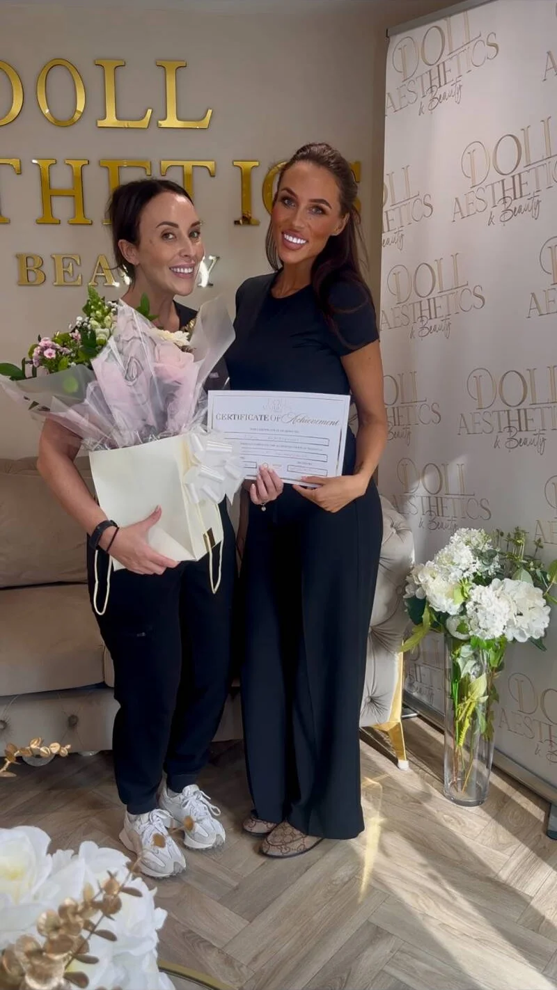 Two Doll Academy graduates holding their certificates and flowers in the clinic